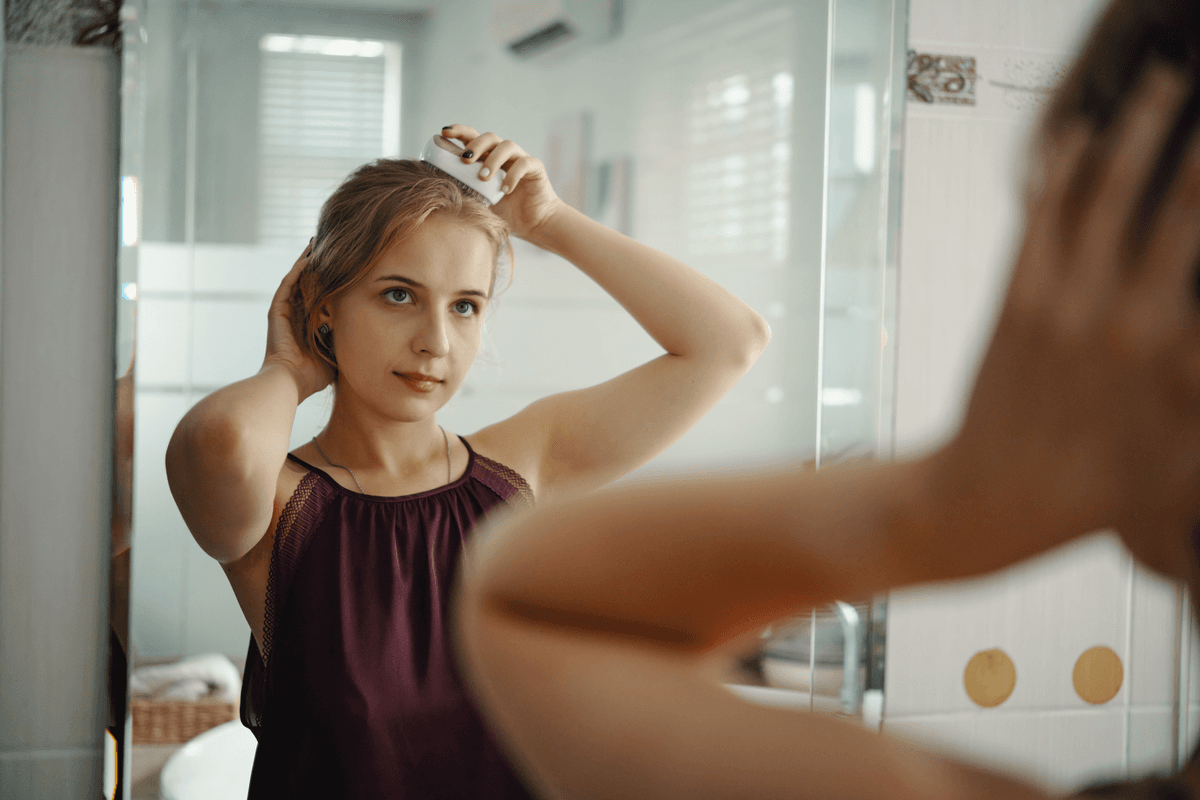 Žena si češe a prohlíží vlasy před zrcadlem v koupelně