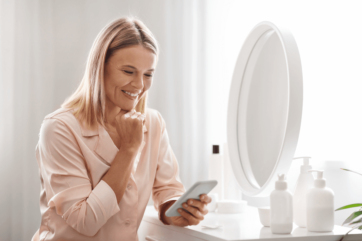 Žena si u zrcadla prohlíží fotografii své pleti v mobilu