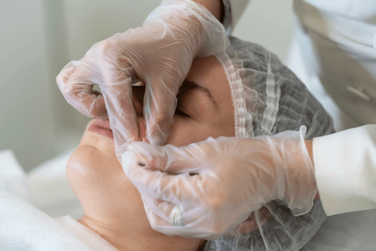 Ruce v rukavicích ošetřují okolí oka klientky v klinickém prostředí